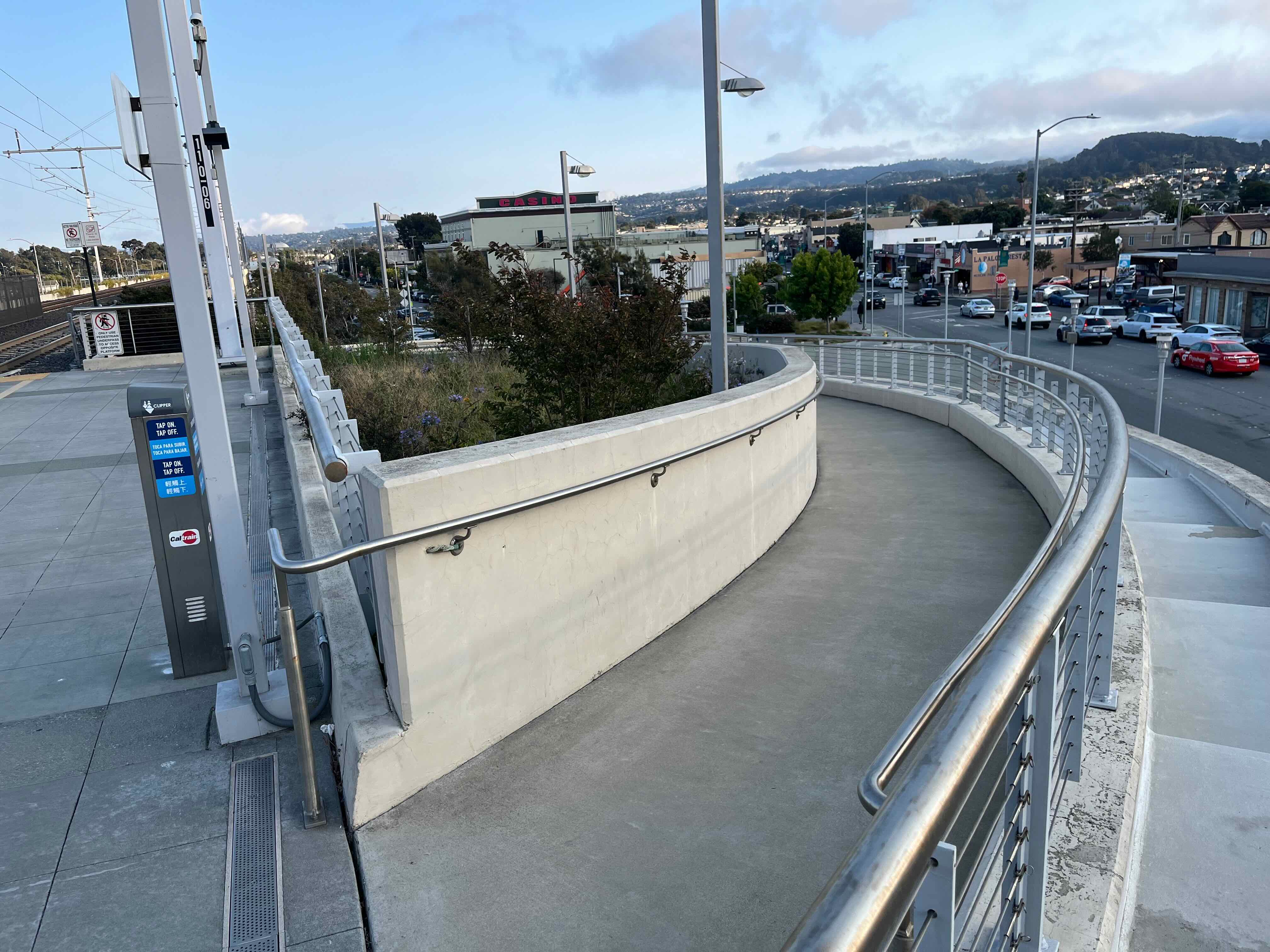 The top of a curving concrete ramp leading down toward street level from a platform..