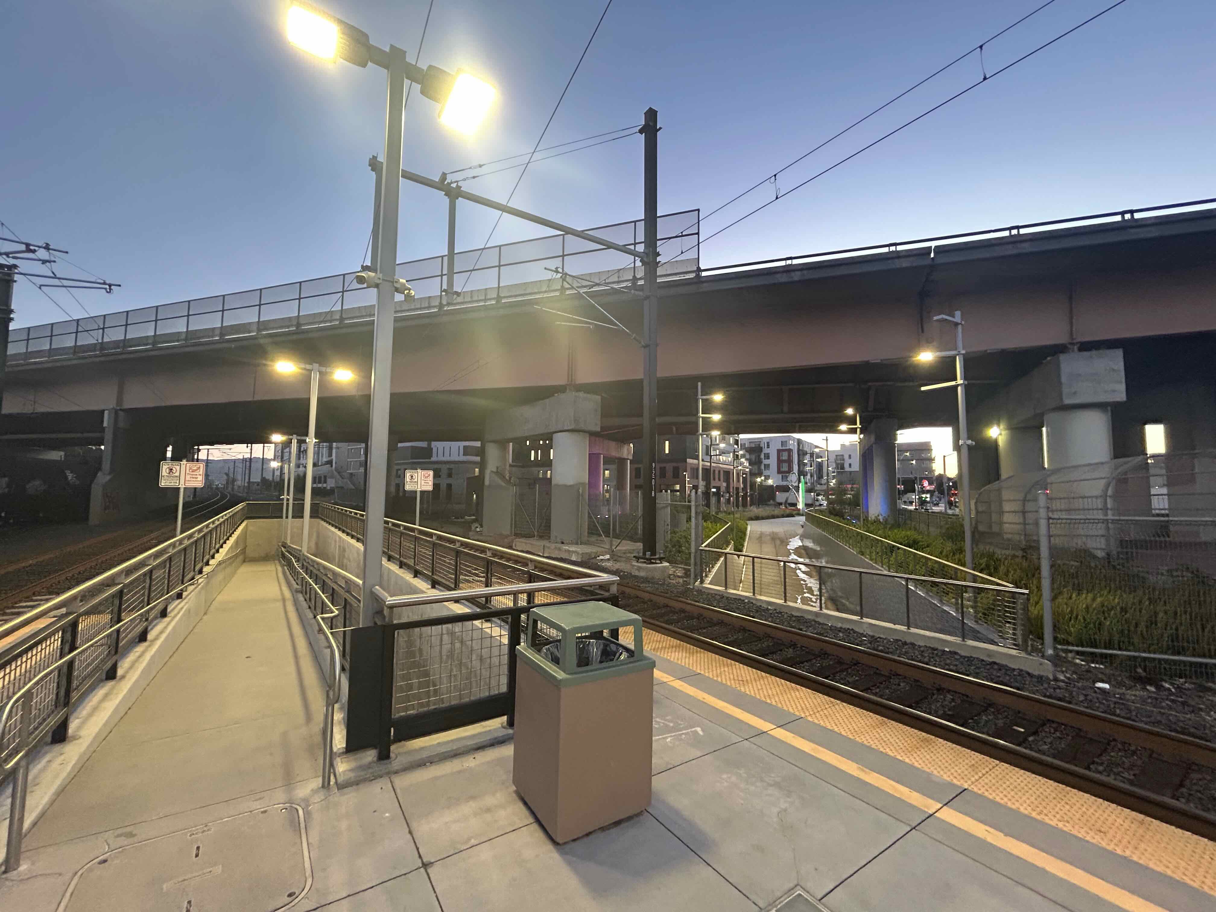 The end of a platform between two tracks. At the end, a narrow ramp descends into the ground, and has a 180degree switchback. To the right, a ramp from a street intersection descends under the tracks. This shows the two ramps that people can use to get between downtown and the platform.